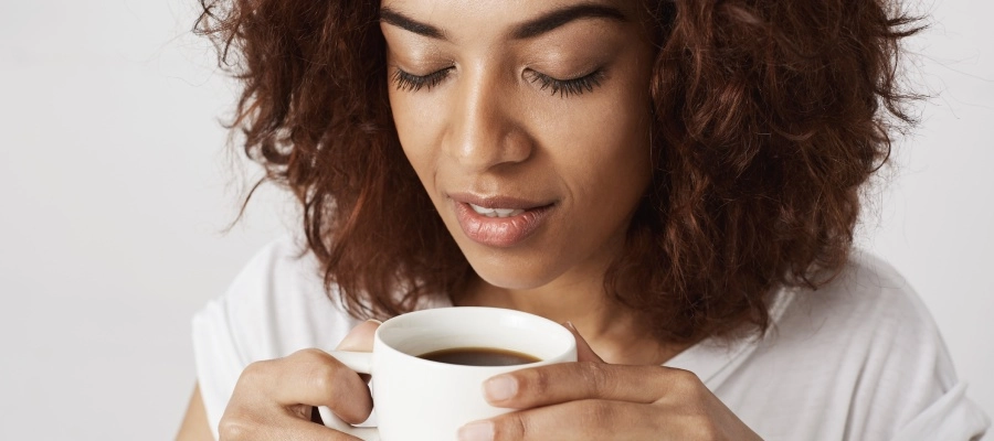 Mulher negra com os olhos fechados, segurando uma xícara de café
