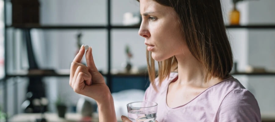mulher segurando um copo d’água e um comprimido em cada mão