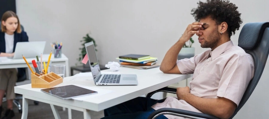 homem cansado em frente ao computador, sem foco e com a mão na testa