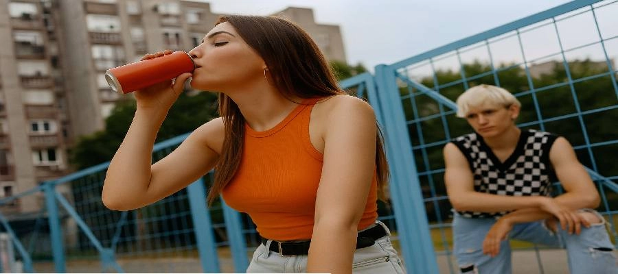 Jovem de blusa laranja bebendo lata de energético