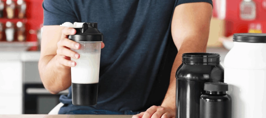 homem branco de blusa preta segura copo com suplementos