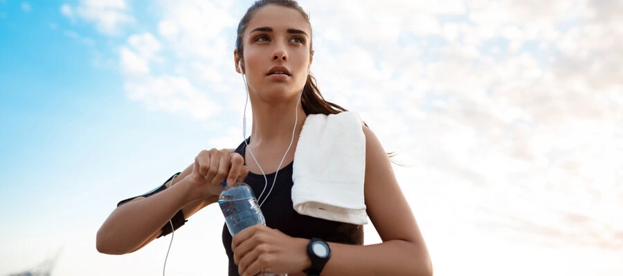 mulher jovem com roupas esportivas se exercitando e segurando uma garrafa de bebida na mão.
