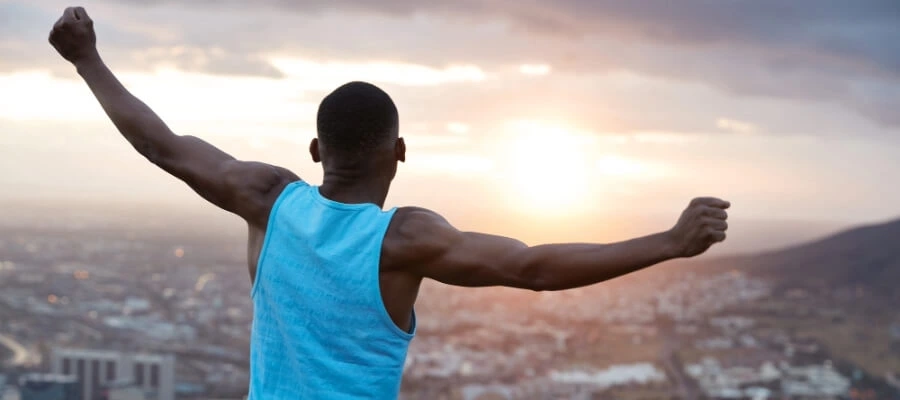 Homem com porte atlético e braços estendidos com vista panorâmica e nascer do sol