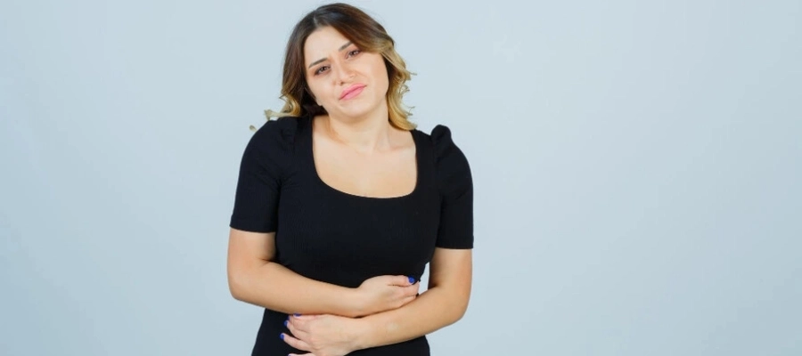 mulher loira com blusa preta e as mãos na barriga sentindo desconforto