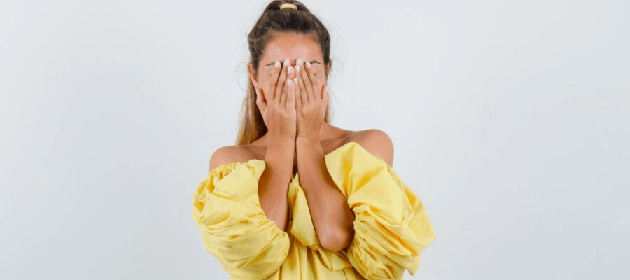 mulher jovem de blusa amarela com as mãos escondendo o rosto sentindo vergonha