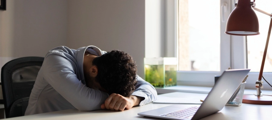 Homem em frente ao computador, aparentando cansaço no local de trabalho.