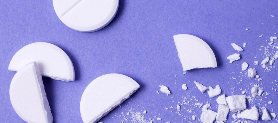 comprimidos brancos inteiro e esmagados sobre um fundo roxo.
