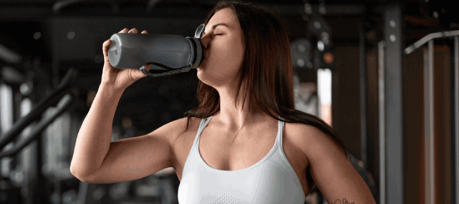 mulher branca de top branco bebe água na academia